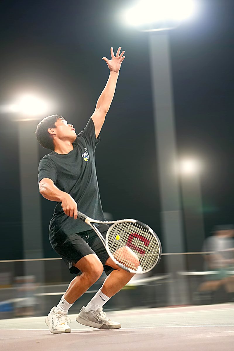 Isaac Lee serving during a night match under floodlights